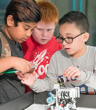 Three boys work on LEGO robot together