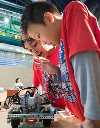 Two students in red shirts look down at LEGO robot